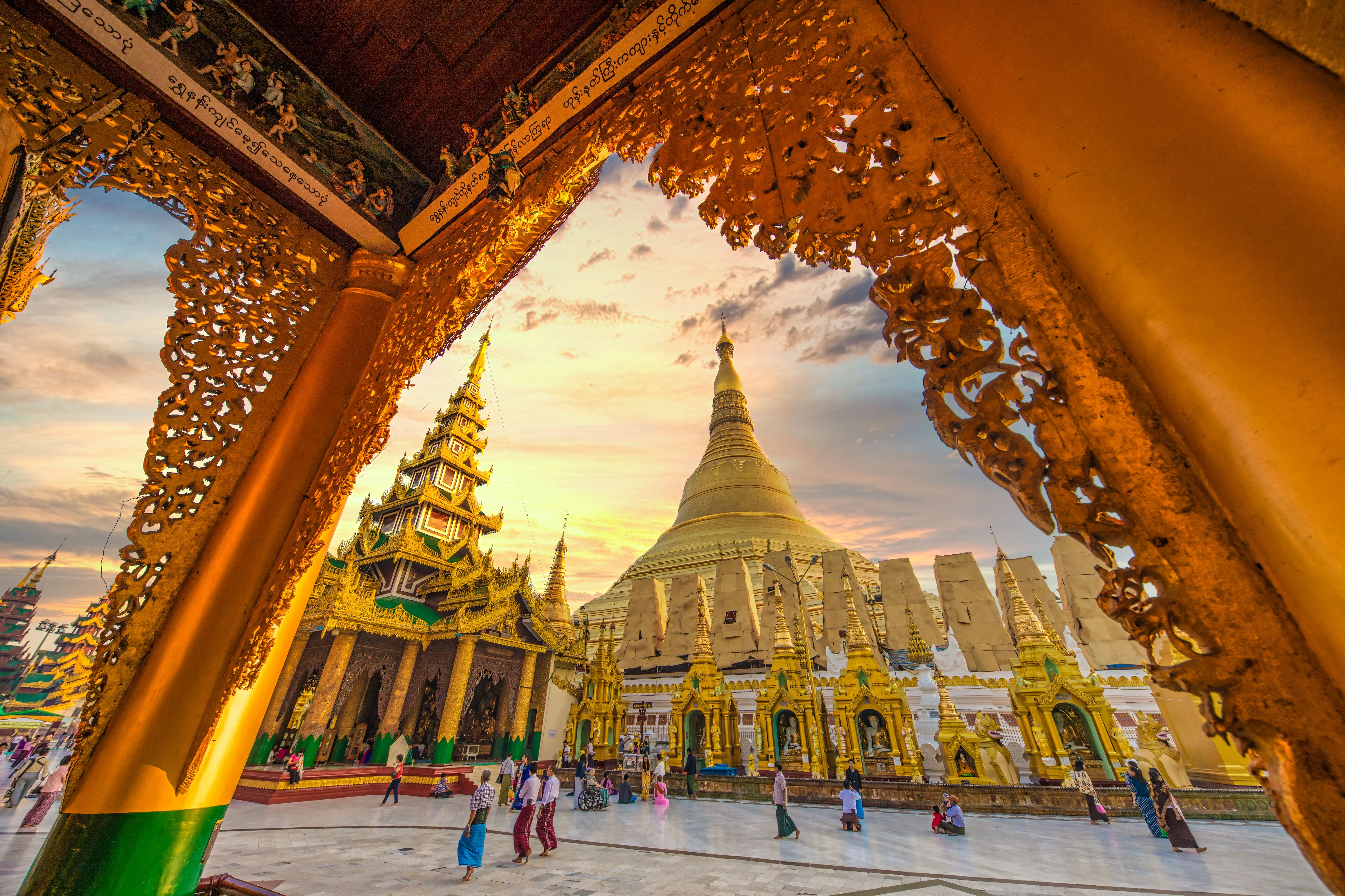 The Shwedagon Pagoda in Yangon at sunset, framed by a carved golden archway